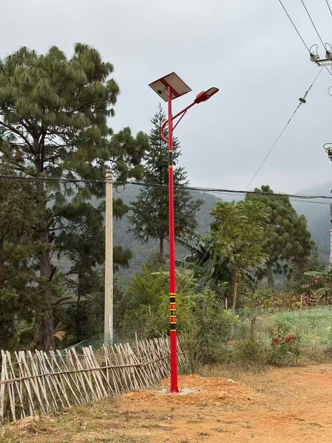 Split-type solar street light on a red pole: panel bolted at the pole top, battery and wiring below the panel, LED luminaire on the arm
